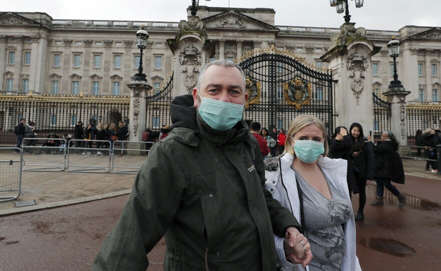 A couple wear face masks as they visit Buckingham Palace in London on Saturday. After criticism for responding slowly, the United Kingdom has urged the public to avoid unnecessary contact.