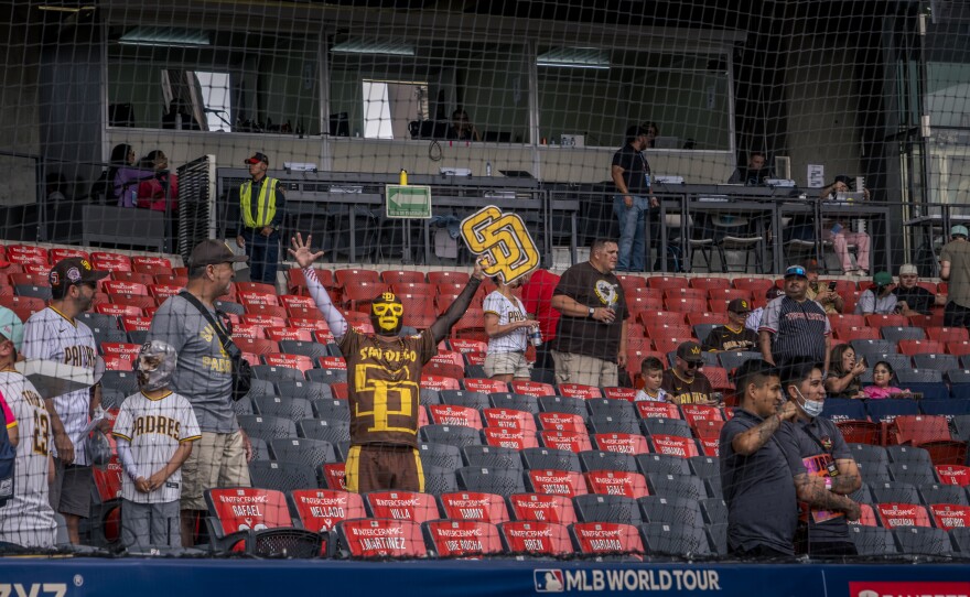 A San Diego Padres fan wearing a yellow and brown luchador mask holds up an SD pendant at Estadio Alfredo Harp Helú, Mexico City, April 29, 2023.