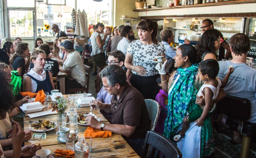 Minara Begum (foreground, far right), holds her daughter Laki while talking to customers at the first Bandhu Gardens pop-up dinner at Rose's Fine Food, a women-owned diner in Detroit, in July 2016.