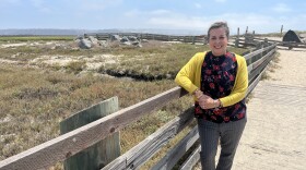 Playwright Mabelle Reynoso leans against a wooden fence at the Tijuana River Estuary, Aug. 20, 2025.