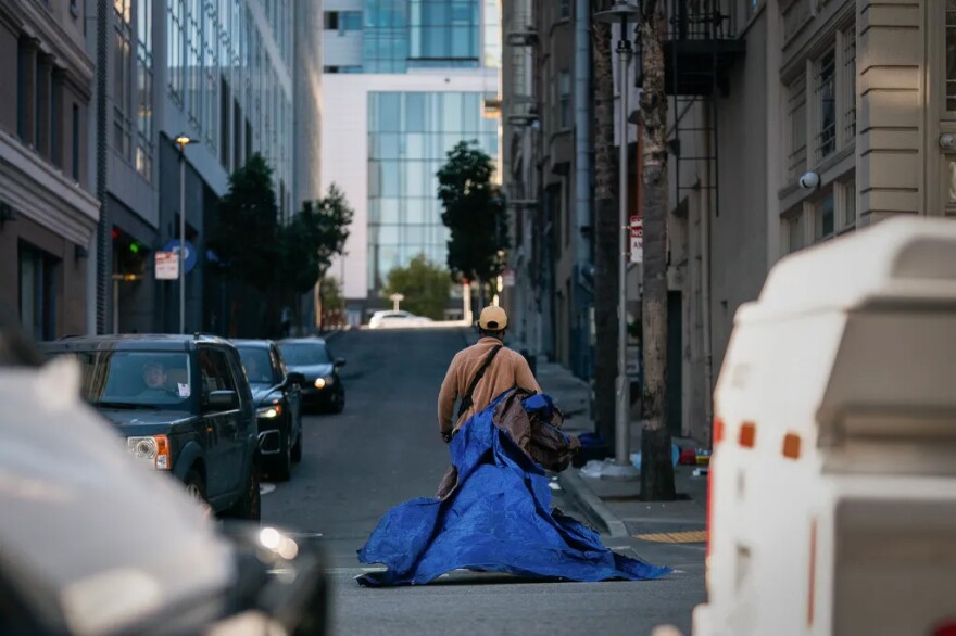 An unhoused man carries a tarp and some of his belongings across Polk Street during a homeless encampment sweep in San Francisco on Nov. 15, 2024. Unhoused people on Cedar Street are forced to move their shelters and belongings on a regular basis by San Francisco city workers.