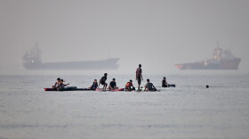 People gather on paddleboards in shallow water as cargo and service vessels are anchored in the Strait of Hormuz off Bandar Abbas, Iran, Monday, June 1, 2026.
