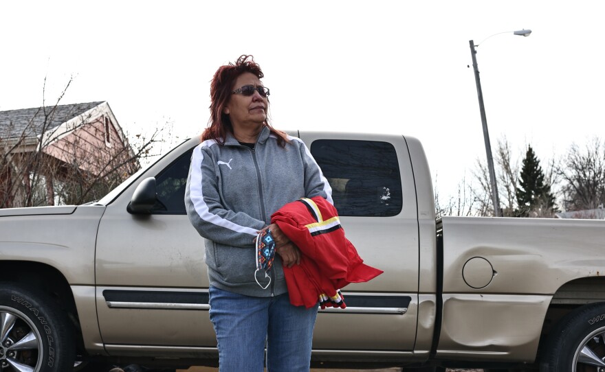 Jo Lynn Little Wounded holds her nephew Waylon's ribbon shirt beside his pickup truck.
