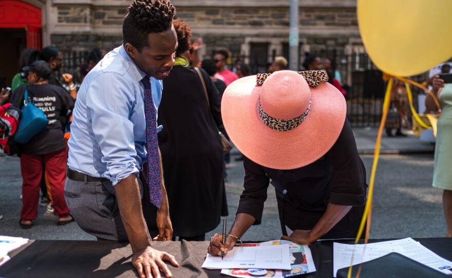 Kolbi Brown (left), a program manager at Harlem Hospital in New York, helps Karen Phillips sign up to receive more information about the All of Us medical research program, during a block party outside the Abyssinian Baptist Church in Harlem.
