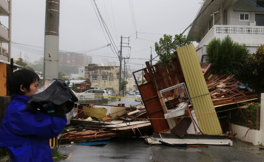 A reporter stands next to a wooden house and restaurant that collapsed across a street due to strong winds from Typhoon Neoguri, in Naha city on the island of Okinawa Tuesday.
