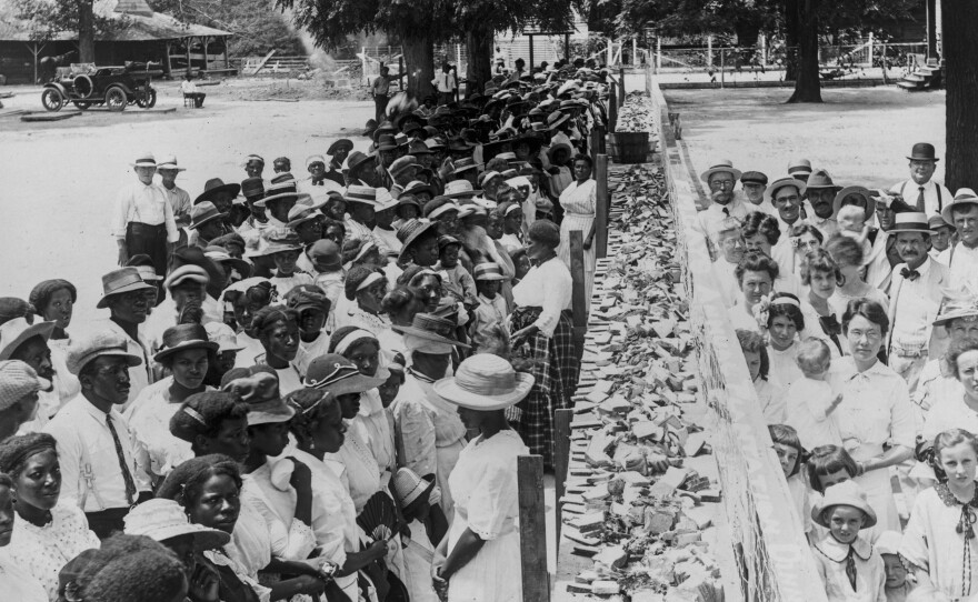 Crowds of African-American and white people are separated by a long counter covered with slices of bread at F.M. Gay's annual barbecue, held on his plantation every year in Alabama.