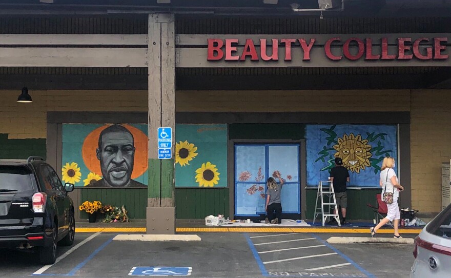 A shopper walks past Chloe Becky's mural of George Floyd while artists continue painting new works on the beauty school storefront on June 2, 2020.