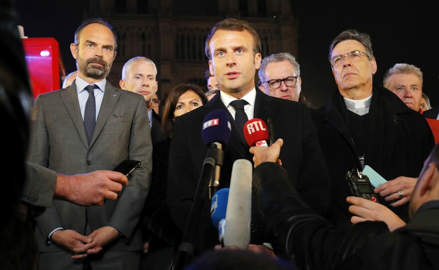 French President Emmanuel Macron speaks as Prime Minister Edouard Philippe and Archbishop of Paris Michel Aupetit stand near the cathedral.