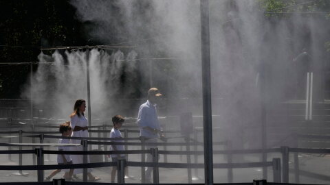 A family walks through a cooling water spray at the Eiffel Tower in Paris, Sunday, June 21, 2026.