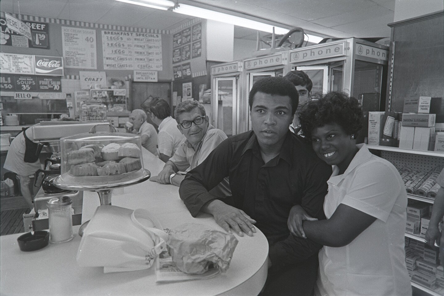 Muhammad Ali seated at a lunch counter, takes picture with fan. Miami, Fla. Feb. 25, 1971.