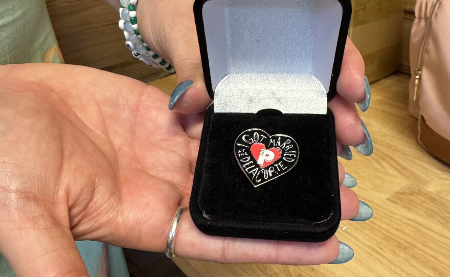 Wedding planner Carla Perez holds up a special pin that the Public had made for each of the couples getting married at the Delacorte.