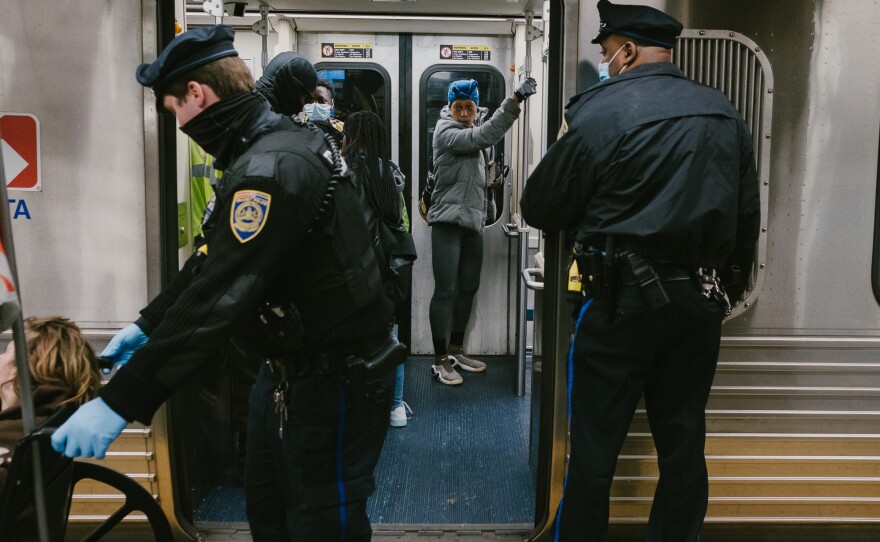 Bires (left) assists a woman onto the train at the 11th Street stop on the Market-Frankford Line.