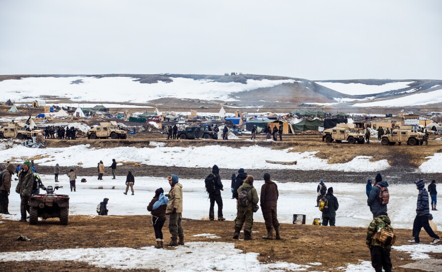Protestors stand on the southern bank of the Cannonball River, on reservation land, as police secure the remainder of the Oceti Sakowin camp on the opposite bank.