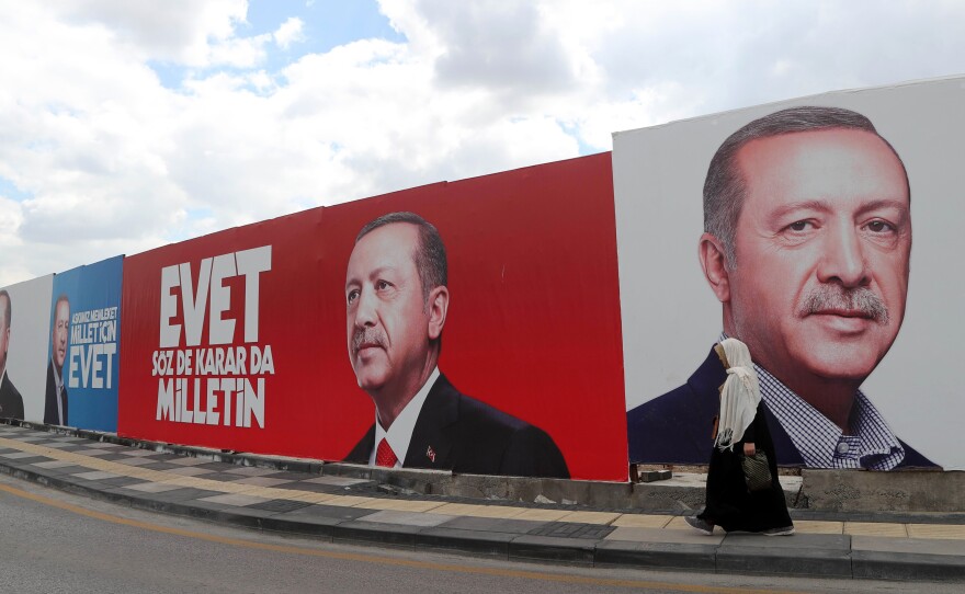 A woman walks past a giant poster bearing portraits of Turkish President Recep Tayyip Erdogan in Ankara, ahead of the referendum on whether to change the current parliamentary system into an executive presidency.