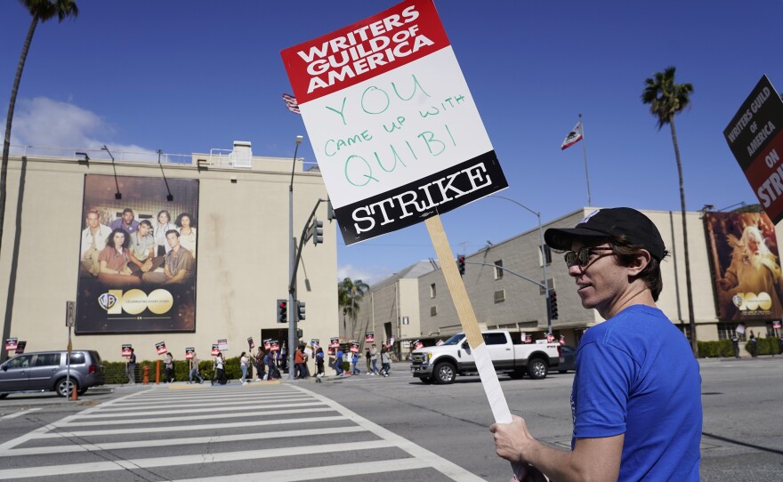 Writer Jono Matt holds a sign referring to the short-lived streaming service Quibi at the WGA picket line outside Warner Bros. Studios in Burbank.