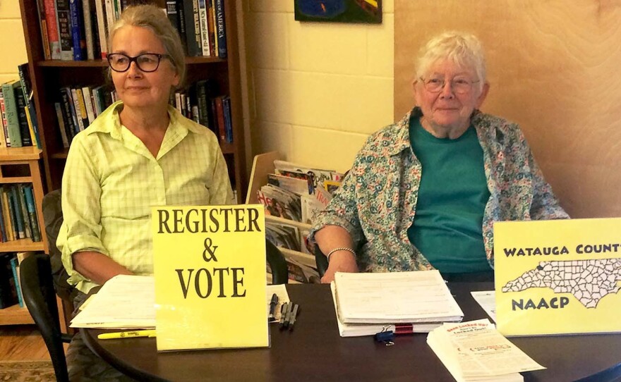 NAACP volunteers Marjorie McKinney (left) and Joan Brannon sit at a booth to register people to vote at the Hospitality House, a community shelter in Boone, N.C.