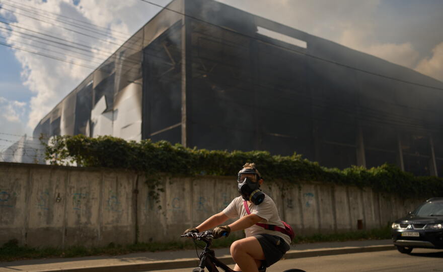 A local resident wears a gas mask as he rides a bicycle past a partially destroyed warehouse after a Russian drone attack in Brovary on the outskirts of Kyiv, Ukraine, Friday, Sept. 4, 2026.