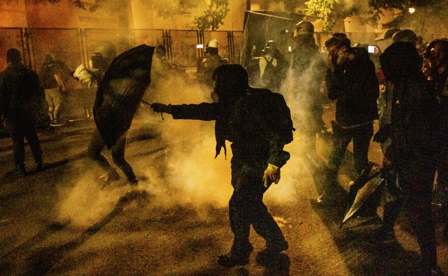 Protesters walk through chemical irritants deployed by federal agents in Portland, Ore. The inspector general of the Justice Department says he is investigating federal officers' roles in responding to protests in Portland and Washington, D.C.