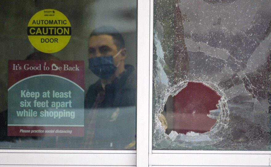 A police officer works behind a broken glass door at the scene where two people were struck by gunfire in a shooting at a Burlington store in North Hollywood, Calif., on Thursday.