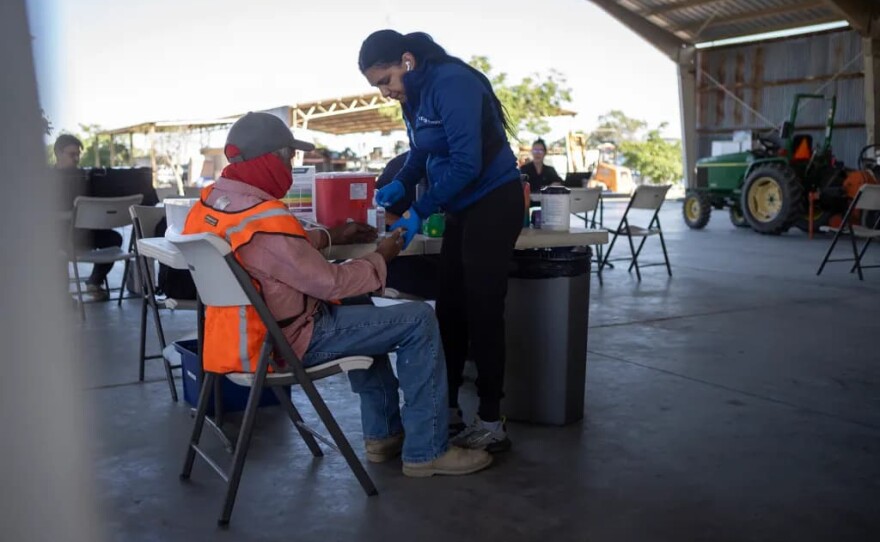 UCSF-Fresno staff member checks the blood sugar of a farmworker during a check-up in an equipment barn during a Rural Mobile Health program visit at a farm outside of Helm on June 16, 2025.