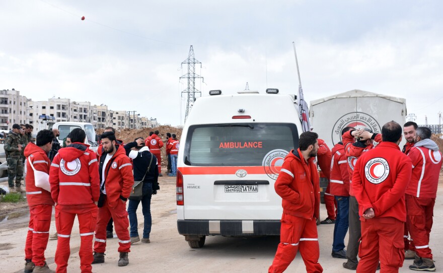 Syrian Red Crescent paramedics wait on Friday for the buses evacuating civilians from the government-held villages of Fuaa and Kafraya, on a highway in eastern Aleppo.