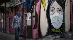A man wearing a face mask walks past a mural Thursday, Oct. 1, 2020, in South Central Los Angeles. California's plan to safely reopen its economy will begin to require counties to bring down coronavirus infection rates in disadvantaged communities that have been harder hit by the pandemic. 