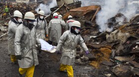 Rescue workers carry a body from the rubble of a village destroyed by the devastating earthquake, fires and tsunami March 16, 2011 in Kesennuma, Miyagi province, Japan. 