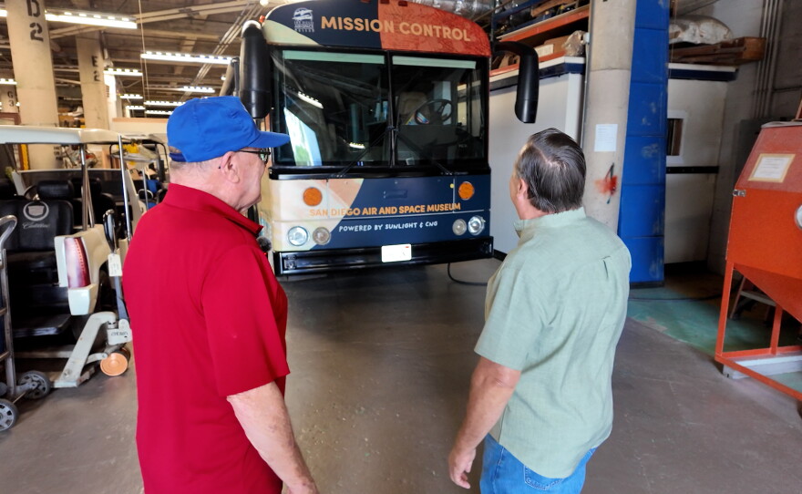 The San Diego Air & Space Museum's "Mission Control" bus is shown with restoration shop volunteer Tom Nolan and KPBS reporter John Carroll in the foreground - at the restoration shop on July 13, 2026.