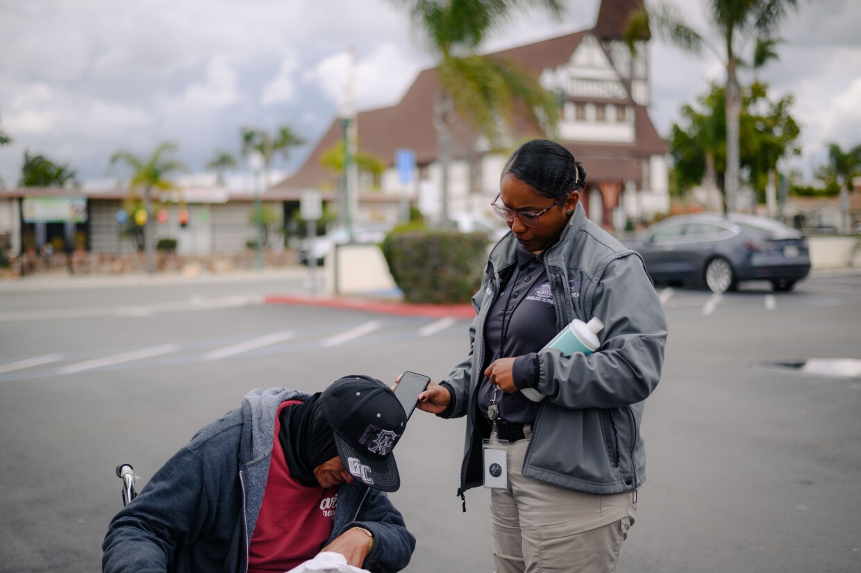 National City HOME team caseworker Qiana Williamson holds her phone so an unhoused resident can speak to a case manager in National City, California on March 7, 2024. National City is the second in San Diego County to move away from a police-led response to homelessness and toward trained caseworkers.
