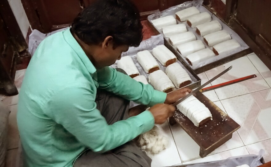 A worker slices rich fruitcake with almond icing at the family-run Saldanha Bakery.