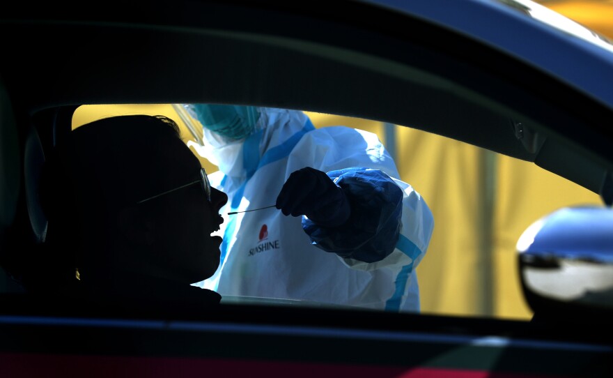 After an initial verbal screening, one driver at a time gets a COVID-19 nasal swab test from a garbed health worker at a drive-up station in Daly City, Calif.