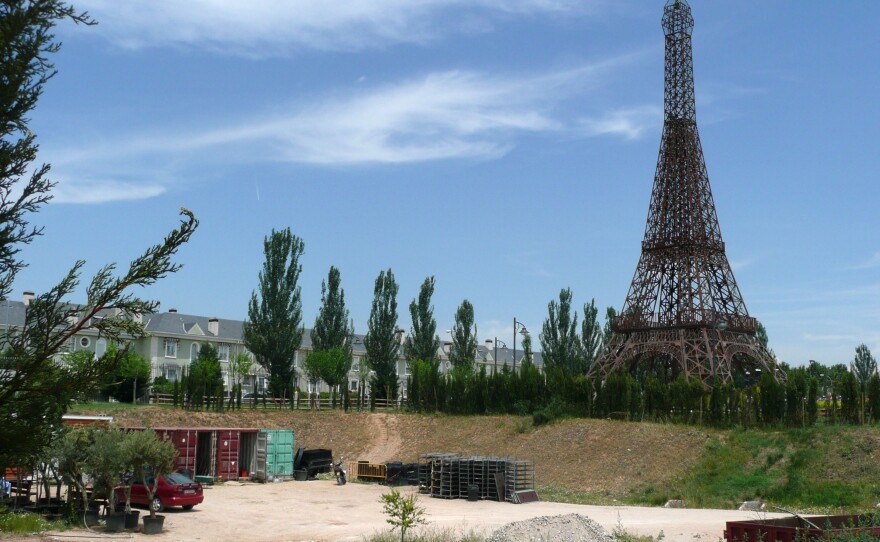 A rusting model of the Eiffel Tower stands at one end of the theme park, surrounded by construction debris and empty housing outside the park.