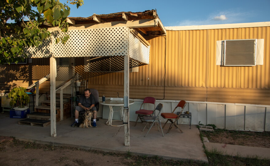 Paul Valdez and his dog, Gunner, sit in the shade outside his home in Tucson, Arizona. The electricity in Valdez's mobile home park has gone off for hours at at time during the hottest parts of the year. Valdez is diabetic, and he worries about heat exposure.