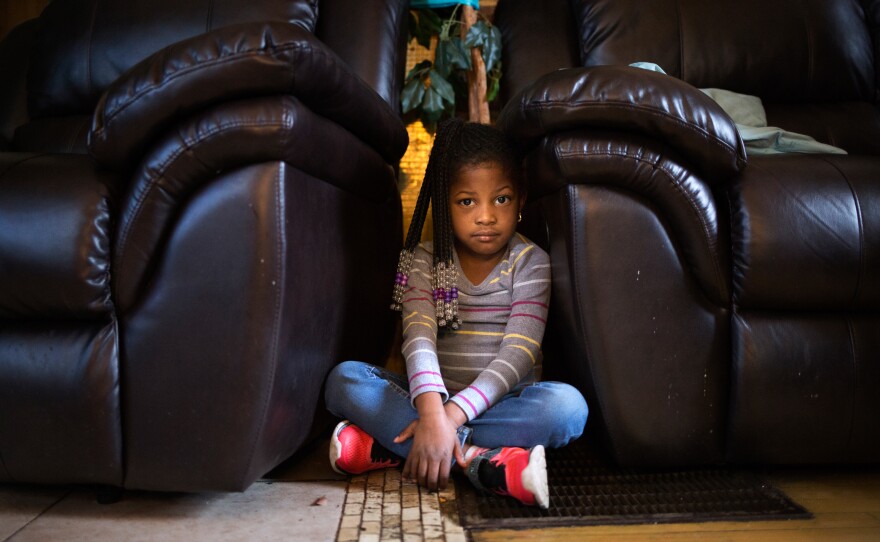 Five-year-old Amor Robinson shows where she went when she heard gunfire outside her grandmother's home in St. Louis. The narrow gap between the couch and armchair recliner became her hideaway.