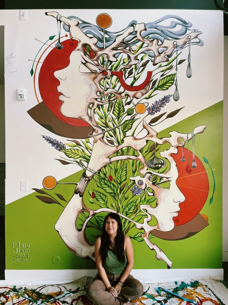 Artist Mary Jhun sitting in front of one of her surrealist murals. Undated photo.