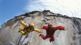 Jean and Carl Boenish in jump down a ledge towards camera.