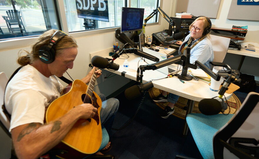 Walsh conducts an interview with musician Matt Fockler, as he plays an acoustic guitar.