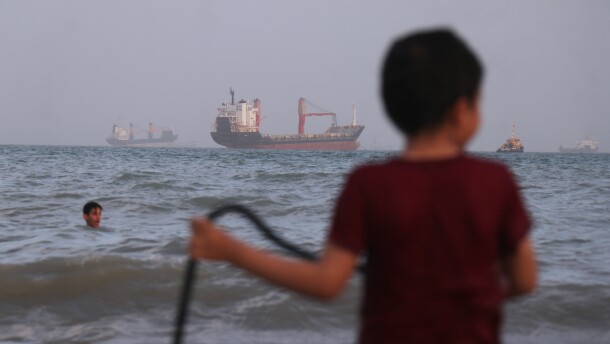 Children play in the water along the shore as a mix of bulk carriers, cargo ships, and service vessels sit offshore in the Strait of Hormuz off Bandar Abbas, Iran, Sunday.