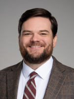 Man smiling with dark hair wearing a tie and suit.