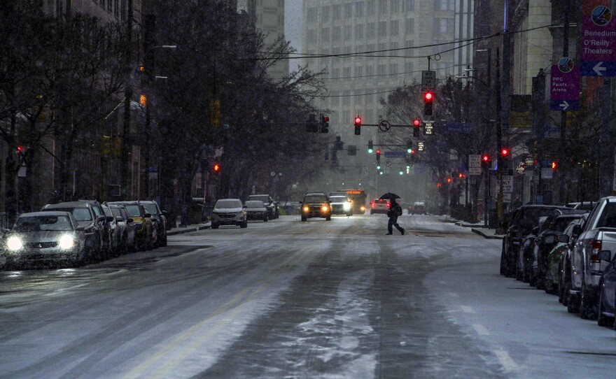 A pedestrian uses an umbrella as they cross Liberty Avenue, in downtown Pittsburgh, as snow begins to fall during a winter storm that will impact the region on Sunday night, Jan. 16, 2022.
