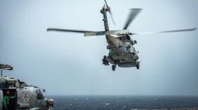 A gray Navy helicopter takes off from the flight deck of the USS Nimitz while deployed as another helicopter sits on the deck.