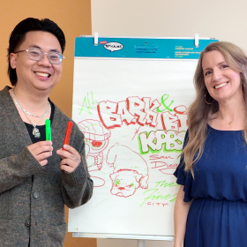 Sign painter and content creator Koy Sun, left, and The Finest host Julia Dixon Evans pose with a drawing Koy created while waiting backstage before KPBS Podcasts Live: The Art of Protest on July 12, 2026.