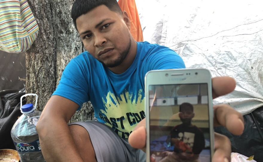 Migrant parents in the tent camps in Matamoros, Mexico, are sending their kids across the border and taking advantage of the rule that unaccompanied children can't be returned to Mexico. Here,  Alexis Martinez holds a cellphone photo of his 7-year-old son Osiel.