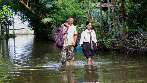 A school girl and her father wade through floodwaters in Alengmora village in Jorhat, India, Monday, Aug. 10, 2026.