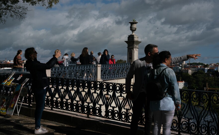 People look at the cityscape at the Miradouro de São Pedro de Alcântara in Lisbon, Portugal.