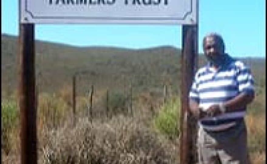 Julius Bozo stands in front of sign of the farm he and other blacks had to leave because of lack of resources and know-how, as well as infighting among the black owners.