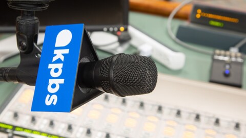 A microphone with a KPBS logo hangs over an audio switchboard in this undated photo.