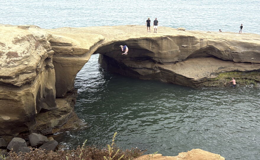 People jump into the water at Pappy's Point in Sunset Cliffs as onlookers watch, Aug. 5, 2026.
