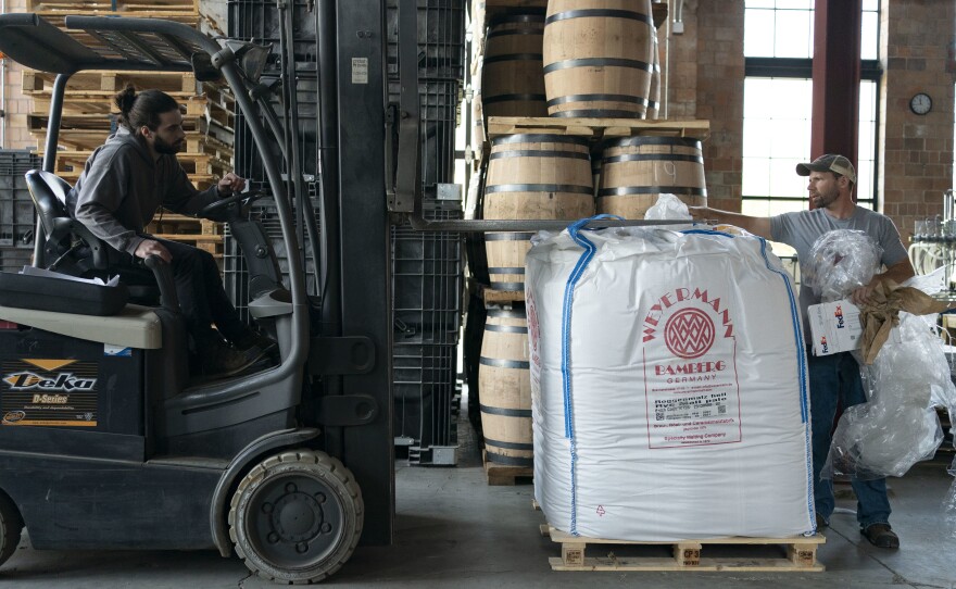 Distillery employee Cody Giles, left, uses a forklift to pick up a container of malt.