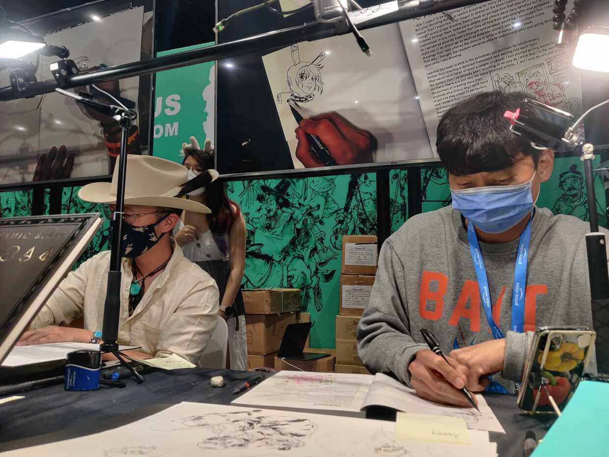 Artist Dongho Kim (right) works on a drawing at a booth in the Comic-Con Exhibit Hall, July 23, 2022.
